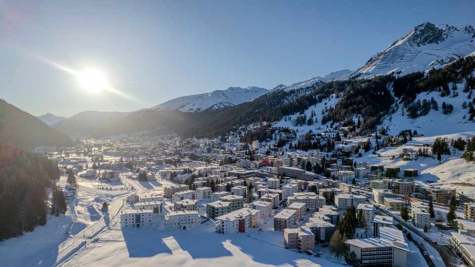 Davos in winter, with snow-covered buildings and mountains in low sunlight