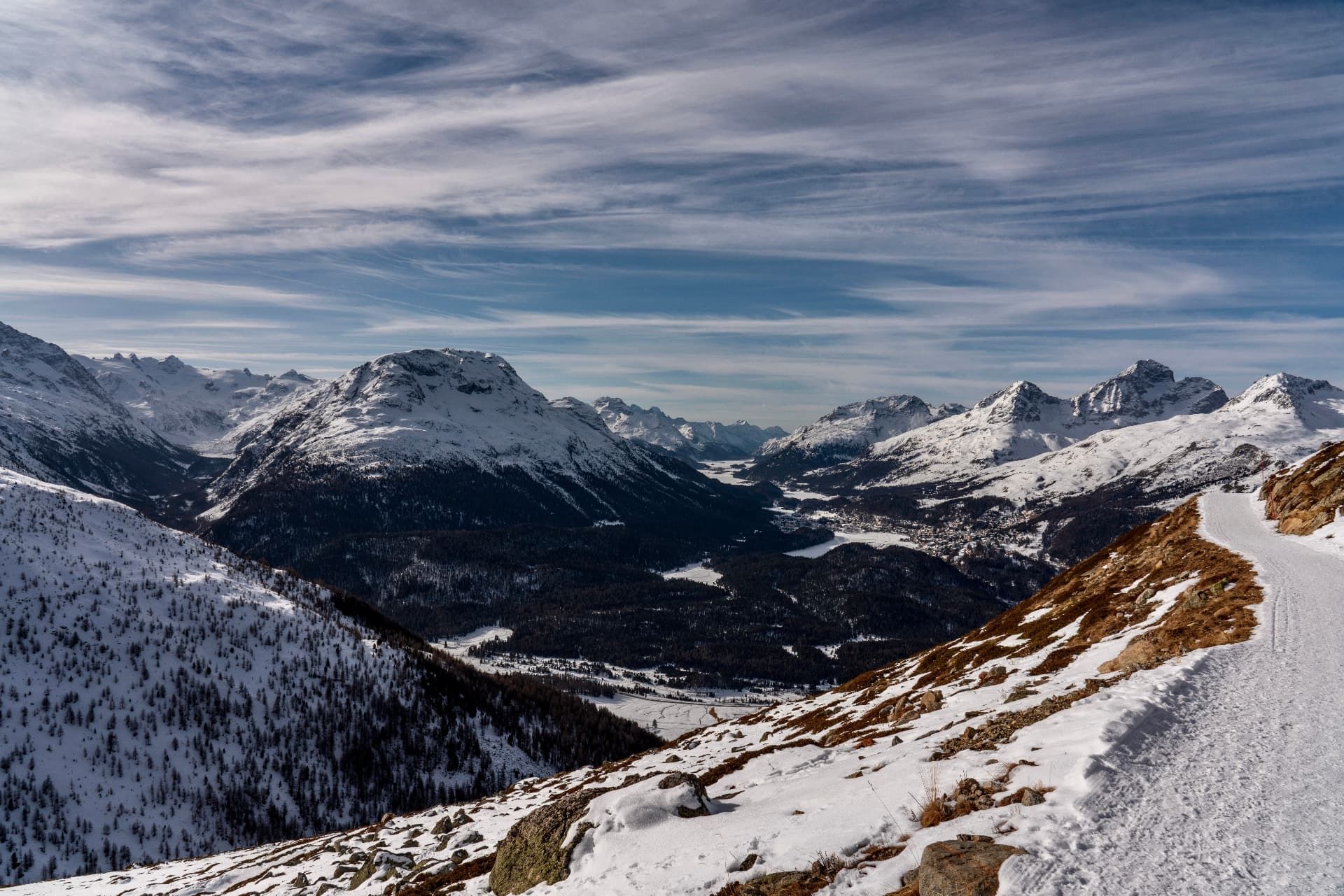 Snow-covered mountains and the Upper Engadin valley near St. Moritz beneath a streaked blue sky