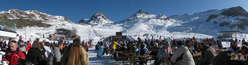 Skiers on a busy Idalp restaurant terrace, with ski lifts and snowy slopes behind them