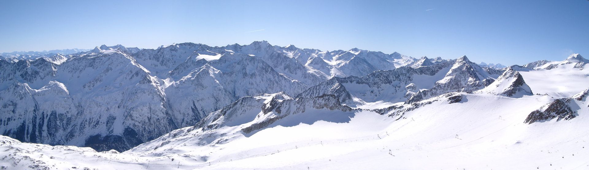 Snow-covered peaks and ski slopes at Sölden’s Tiefenbach glacier beneath a blue sky
