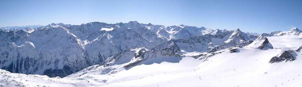Snow-covered peaks and ski slopes at Sölden’s Tiefenbach glacier beneath a blue sky